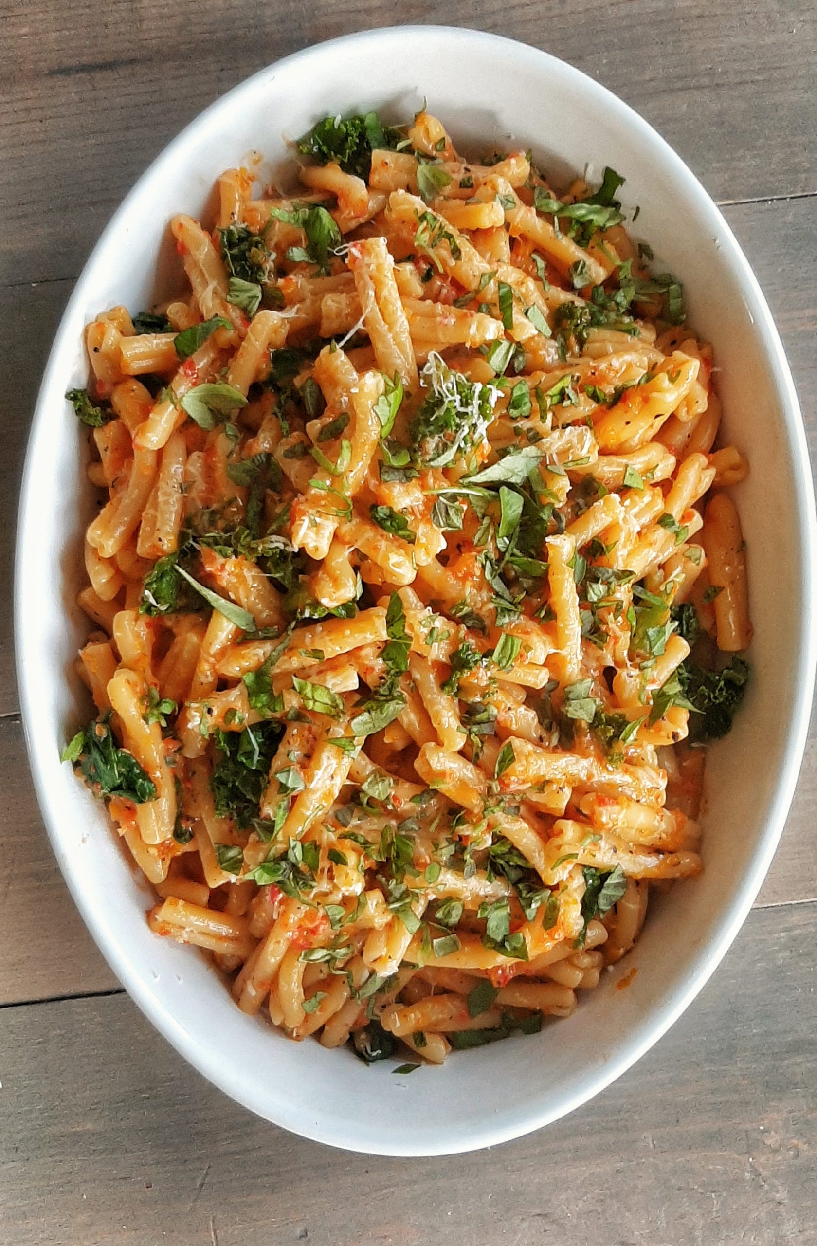 A delicious plate of pasta smothered in a vibrant orange roasted red pepper sauce topped with fresh herbs.